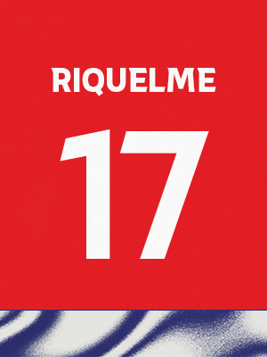 Dorsal de color rojo con el nombre 'Riquelme' y el número 17 en blanco, sobre un borde inferior con patrón ondulado azul y blanco.