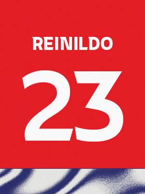 Dorsal de color rojo con el nombre 'Reinildo' y el número 23 en blanco, sobre un borde inferior con patrón ondulado azul y blanco.